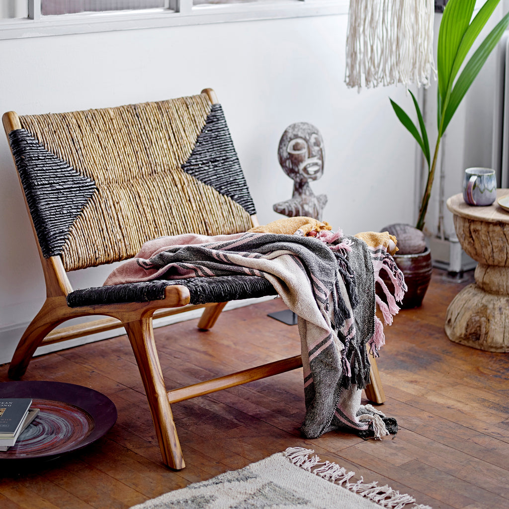 Rattan lounge chair with sofa throw and wooden sculpture of a tribal man